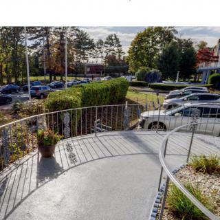 A view of a parking lot with several cars, surrounded by trees and a fenced pathway on a clear day.