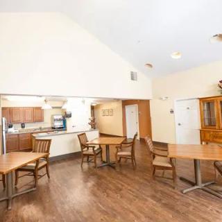 A spacious dining area with wooden floors, featuring several tables and chairs adjacent to an open kitchen.