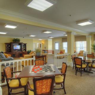A cozy dining and recreational area with multiple tables, chairs, and a seating space illuminated by large windows.