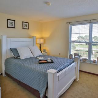 A cozy bedroom with a large window allowing natural light to fill the space, featuring a neatly made bed and warm lighting.