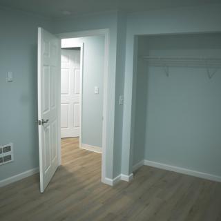 An empty room with an open door and closet, featuring laminate flooring and white walls.