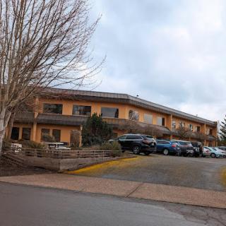 A cozy hotel building with a parking lot under a cloudy sky.