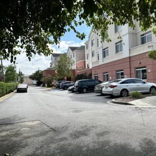A parking lot with several cars in front of a building, surrounded by trees under a partly cloudy sky.