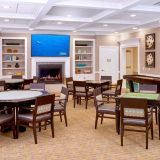 A well-lit dining area with multiple tables and chairs, a fireplace, bookshelves, and decorative art on the walls.