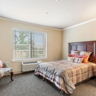 A cozy bedroom with a double bed, patterned bedding, a chair by the window, and ample natural light.