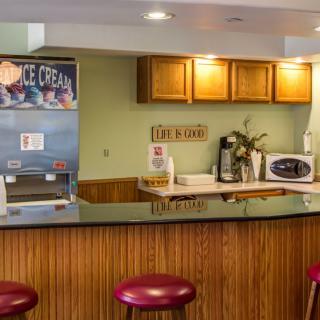 A small kitchen area with a countertop, bar stools, and various appliances including an ice cream machine, coffee maker, and microwave.