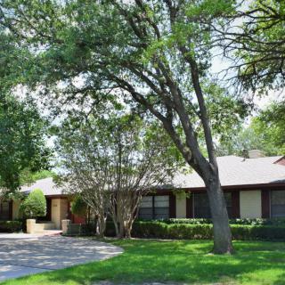 A suburban house with a driveway and lush trees in the front yard.