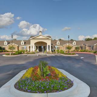 A grand entrance to a building with well-maintained landscaping under a partly cloudy sky.