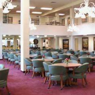 An elegant dining hall with neatly arranged tables and chairs, featuring soft lighting and a plush carpet.