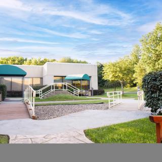 A modern building with green awnings surrounded by landscaped gardens and pathways under a bright blue sky.