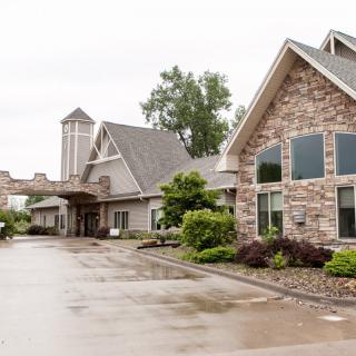 A stone-faced building with a driveway and surrounding greenery on an overcast day.