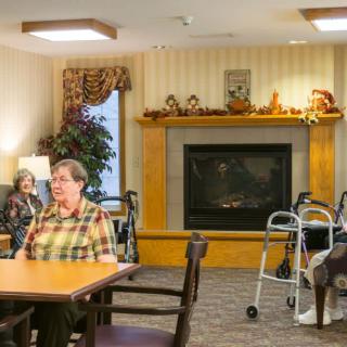 A community room in a nursing home with elderly residents sitting near a fireplace.