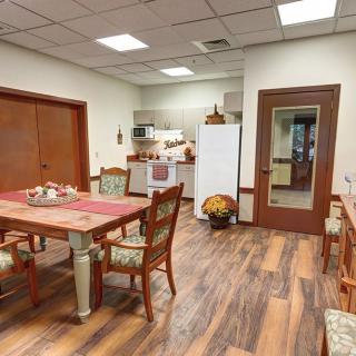 A cozy kitchen and dining area with a wooden table and chairs, featuring a refrigerator and a warm wooden floor.