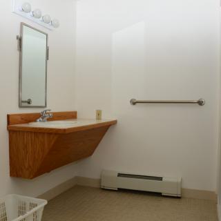 A minimalist bathroom with a wooden sink counter, mirror, and handrail.
