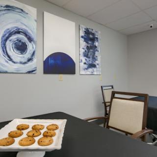 A cozy breakroom featuring a plate of cookies, modern furniture, and abstract artwork on the walls.