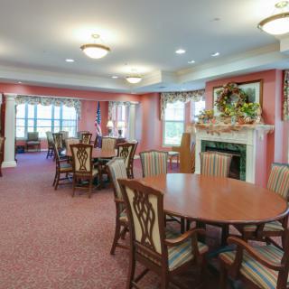 A warmly decorated dining room with multiple tables and chairs, featuring a fireplace and elegant lighting.