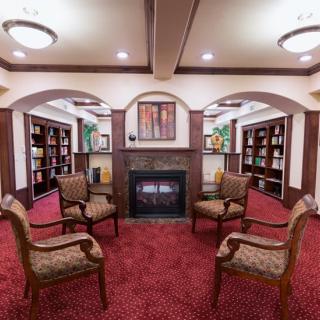 A cozy library interior with chairs arranged around a fireplace, surrounded by bookshelves.