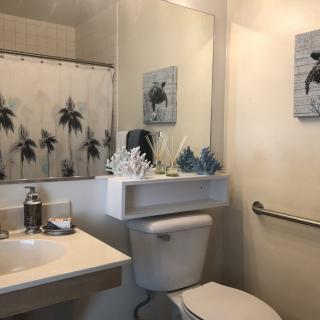 A beach-themed bathroom with palm tree shower curtain, decorative art, and functional fixtures.