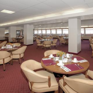 An indoor dining area with neatly arranged tables and chairs, featuring a carpeted floor and place settings.
