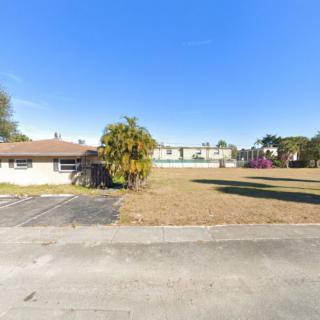 A suburban house with a large lawn and palm trees under a clear blue sky.