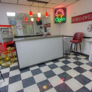 A retro diner featuring a checkered floor, neon signs, and a popcorn machine.