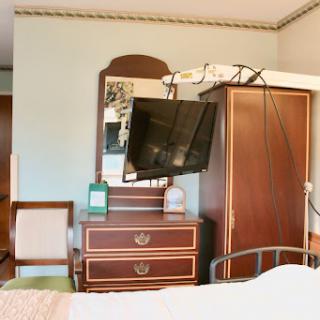A cozy bedroom setup featuring a wall-mounted television, a mirror, and wooden furniture.