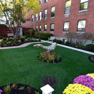 A beautifully landscaped garden with vibrant flowers and a green lawn in front of a brick building.