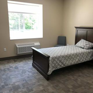 A minimalist bedroom with a single bed, chair, and window.