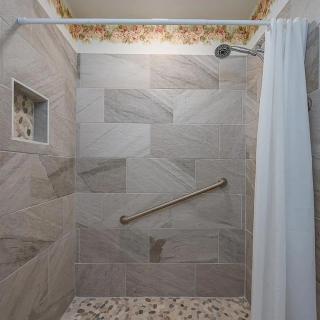 A modern shower with large tiles, a grab bar, and a white shower curtain.