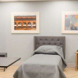 A minimalist bedroom featuring a neatly made bed, elegant artwork on the walls, and a calming green color scheme.