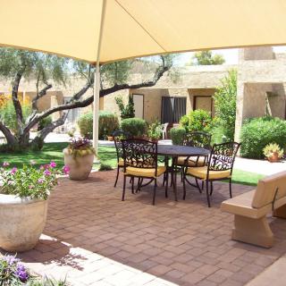 A cozy patio with outdoor seating under a shade sail, surrounded by lush greenery.