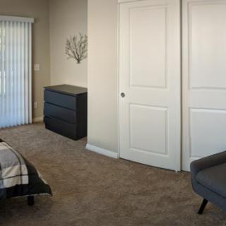 A tidy bedroom with a dresser, chair, and closet doors.