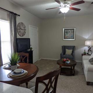 A cozy living room with a sofa, armchair, and coffee table, featuring a TV and decorative elements.