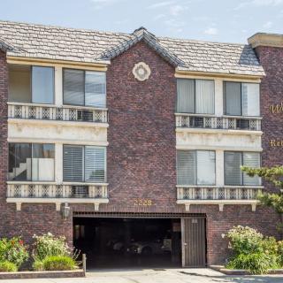 A three-story brick apartment building with large windows and a garage entrance, surrounded by landscaped greenery.