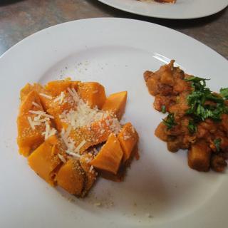 A plate featuring pumpkin gnocchi topped with Parmesan cheese and a side of savory stew garnished with fresh herbs.