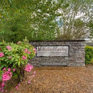 Entrance sign surrounded by lush greenery and blooming flowers.