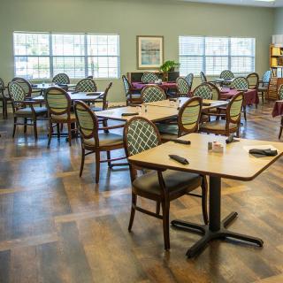An inviting dining area with neatly arranged tables and chairs, featuring large windows that let in natural light.