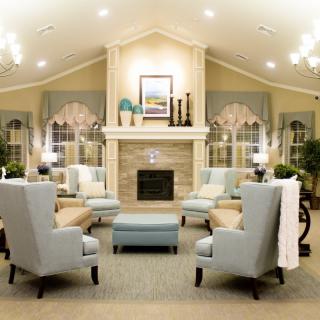 A spacious and elegantly decorated living room featuring a central fireplace, comfortable upholstered seating, and ambient chandelier lighting.