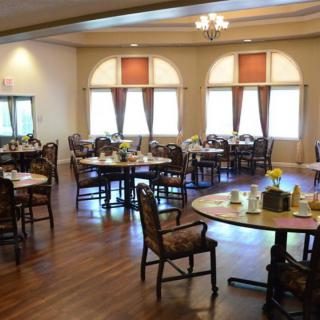 A spacious dining area with neatly arranged tables and chairs on a wooden floor, well-lit by natural light from the windows.