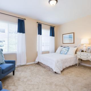 A bright and inviting bedroom with a comfortable bed, blue accent chair, and large windows.