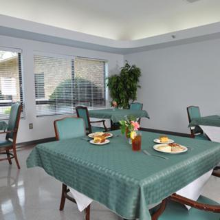 A well-lit dining area with tables set for a meal, featuring green tablecloths and floral centerpieces.