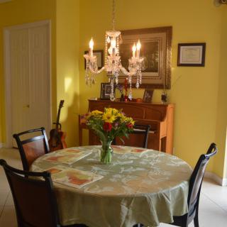 A cozy dining room with a round table, chandelier, and a piano against yellow walls.