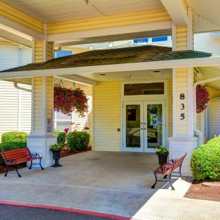 A welcoming building entrance with an awning, surrounded by benches and well-maintained landscaping.