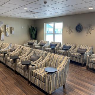 A modern lounge area with striped chairs arranged in a row, featuring small round tables and contemporary wall art.