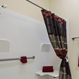 A bathroom with a colorful shower curtain, red towels, and a grab bar for safety.