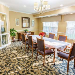 A well-lit dining room with a long table, surrounded by chairs and adorned with a chandelier.