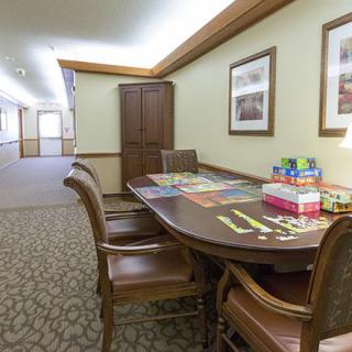 A cozy interior setting with a table and chairs, featuring board games and framed artwork on the walls.