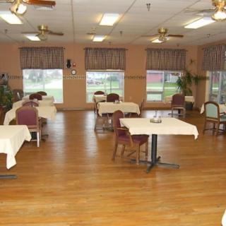 An empty dining room with tables and chairs, featuring wooden flooring and large windows.