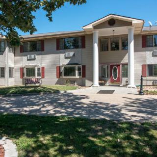 A two-story residential building with prominent columns, surrounded by trees and a well-maintained lawn.