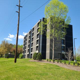 A modern apartment building set against a clear blue sky, surrounded by lush greenery.
